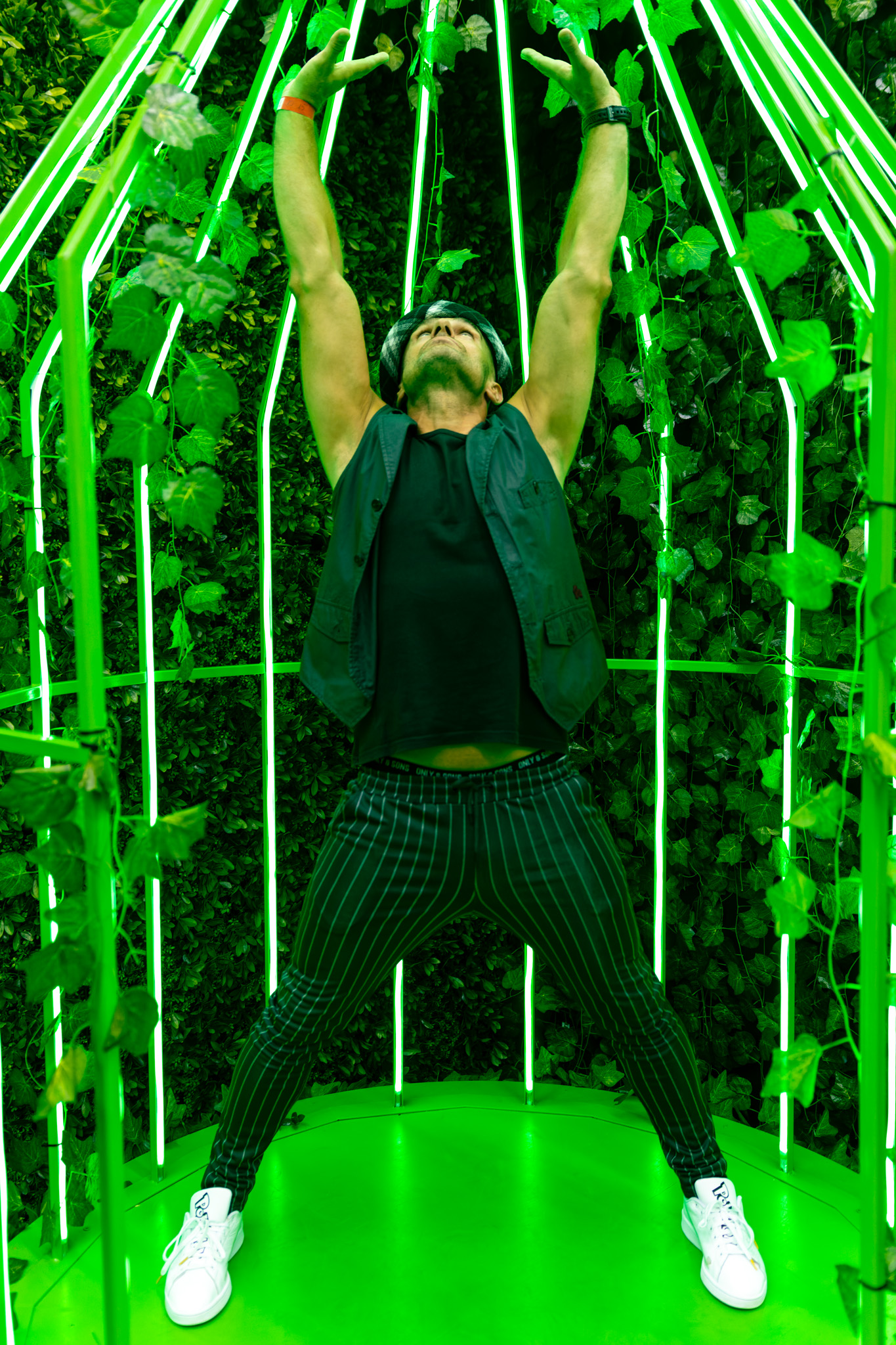 Mężczyzna stojący w rozkroku z uniesionymi rękami na zielonym tle.